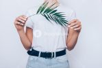 storyblocks-slender-young-woman-wearing-blue-high-waist-jeans-with-belt-and-plain-t-shirt-standing-over-white-background-holding-green-palm-leaf-close-up_rmUjoBxB7_SB_PM.jpg